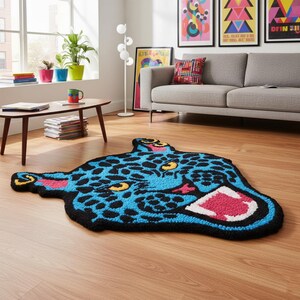 May include: A blue and black rug in the shape of a jaguar's head. The rug features a blue background with black spots, yellow eyes, and a pink mouth. The rug is placed on a wooden floor in a living room setting.