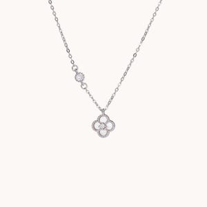 May include: A silver necklace with a four-leaf clover pendant. The pendant and chain are embellished with small gemstones. The necklace is shown against a plain, light background, emphasising its elegant design. The chain is delicate.