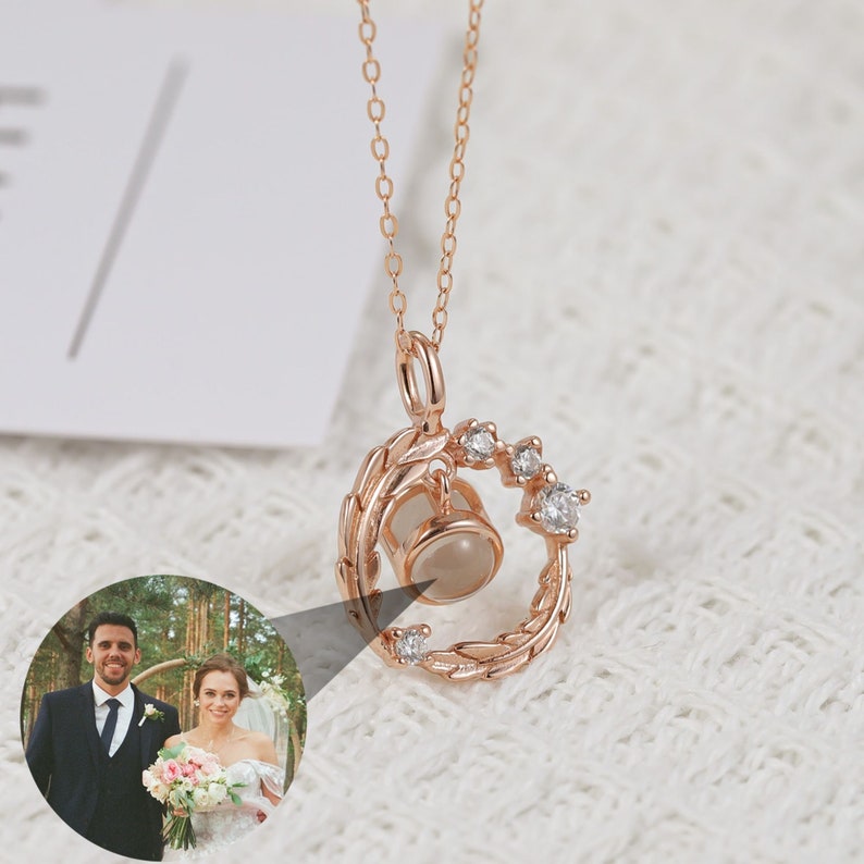 Puede incluir: Un collar de oro rosa con un colgante circular que presenta un peque&ntilde;o inserto para fotos y un delicado dise&ntilde;o de hojas. El colgante est&aacute; acentuado con peque&ntilde;as piedras de circonita c&uacute;bica transparentes.