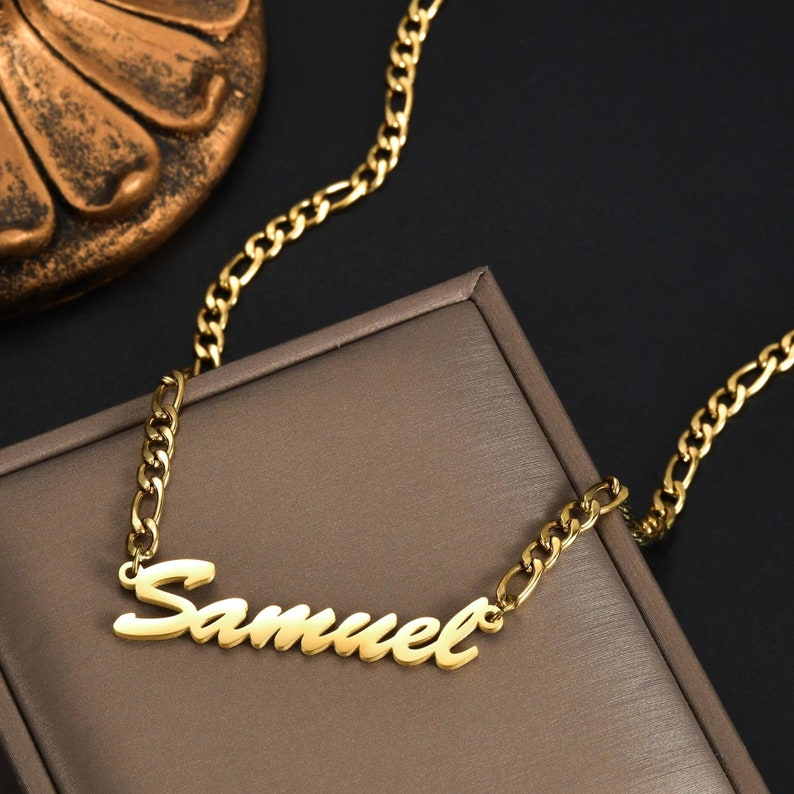 Pu&ograve; includere: Una collana color oro con un ciondolo a forma di targhetta con il nome Samuel scritto in corsivo. Il ciondolo &egrave; fissato a una catena color oro in stile figaro, composta da un motivo di tre maglie circolari piccole e una maglia ovale allungata.