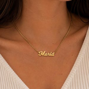 Pu&ograve; includere: Una collana in metallo color oro con una sottile catena a maglie e un ciondolo centrale. Il ciondolo riporta il nome Maria in un carattere corsivo. La collana poggia sul collo e presenta una finitura lucida e riflettente.