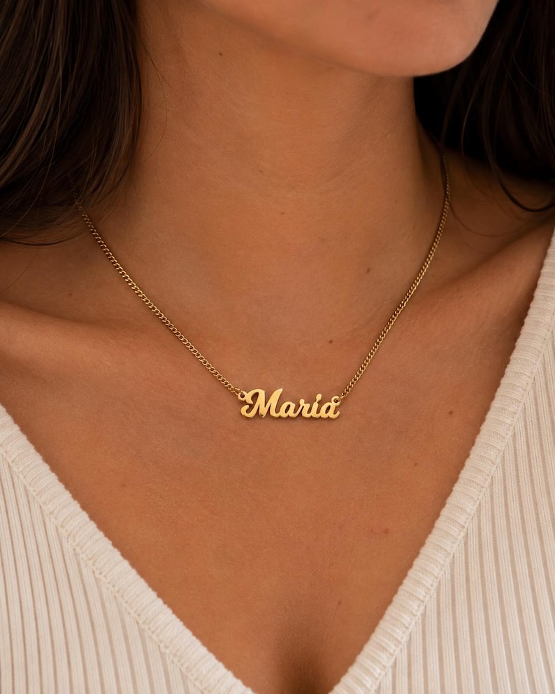 Pu&ograve; includere: Una collana in metallo color oro con una sottile catena a maglie e un ciondolo centrale. Il ciondolo riporta il nome Maria in un carattere corsivo. La collana poggia sul collo e presenta una finitura lucida e riflettente.
