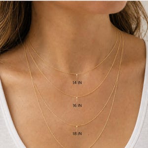 Pu&ograve; includere: Una guida alla lunghezza delle catenine in oro con quattro catene sottili da 14, 16, 18 e 20 pollici. Il testo recita CHAIN LENGTH GUIDE e Includes a 2" extender for adjustable length. Ogni catena ha un piccolo pendente verticale al centro.