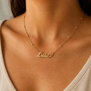Pu&ograve; includere: Una collana color oro con una catenina sottile decorata da piccole perline metalliche distanziate uniformemente. Il ciondolo centrale riporta il nome Lucia in carattere corsivo, completato da una piccola icona a forma di cuore.