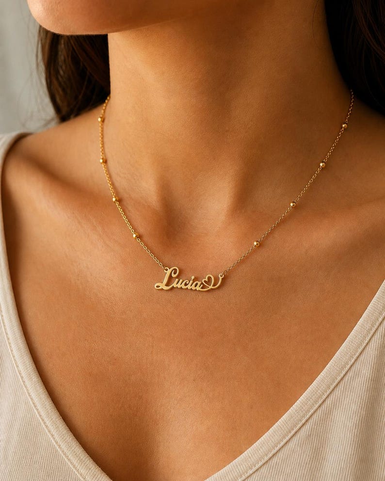 Pu&ograve; includere: Una collana color oro con una catenina sottile decorata da piccole perline metalliche distanziate uniformemente. Il ciondolo centrale riporta il nome Lucia in carattere corsivo, completato da una piccola icona a forma di cuore.