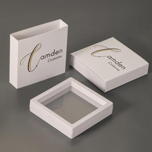 Pu&ograve; includere: Due scatole espositive quadrate bianche e una custodia bianca, ciascuna con il testo nero e oro Camden Customs e una C stilizzata. Le scatole presentano una finestra centrale trasparente che permette di vedere attraverso la cornice e una finitura opaca.