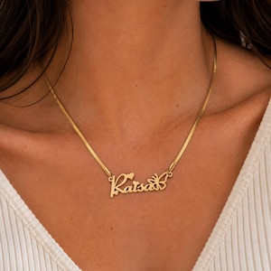 Pu&ograve; includere: Una collana color oro con una catena piatta a spina di pesce e un ciondolo con nome personalizzato che riporta la scritta Raisa in corsivo. Il ciondolo include un piccolo cuore sopra la lettera i e una sagoma di farfalla sul lato destro.