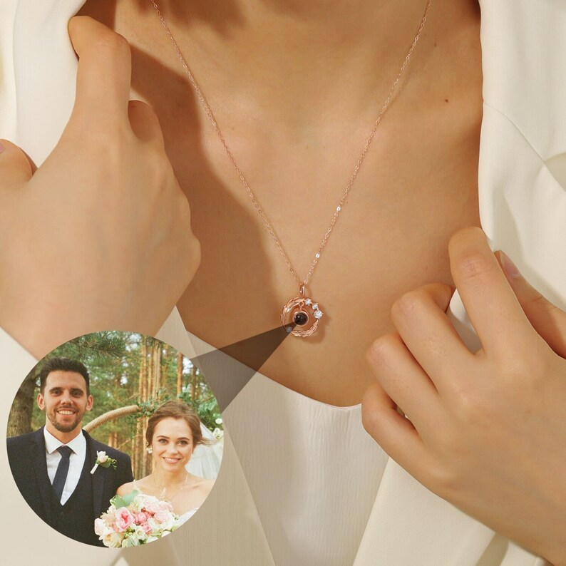 Puede incluir: Un collar de oro rosa con un peque&ntilde;o colgante redondo que proyecta un mensaje cuando se ve a trav&eacute;s de una lupa. El colgante est&aacute; adornado con peque&ntilde;as piedras transparentes.