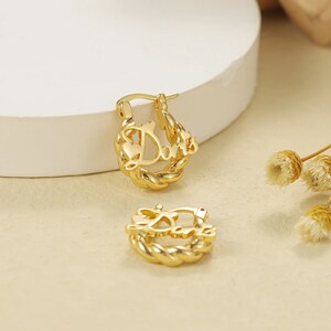 May include: Gold hoop earrings with the word "Dani" written in a cursive font.