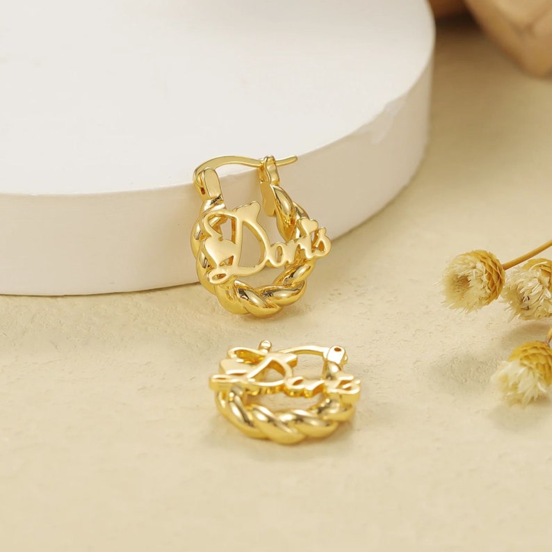 May include: Gold hoop earrings with the word "Dani" written in a cursive font.