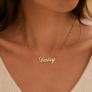 Pu&ograve; includere: Una collana in metallo color oro con un ciondolo a forma di targhetta con il nome Daisy scritto in un carattere corsivo. Il ciondolo &egrave; fissato a una delicata catenina color oro che poggia attorno al collo, con una finitura lucida.