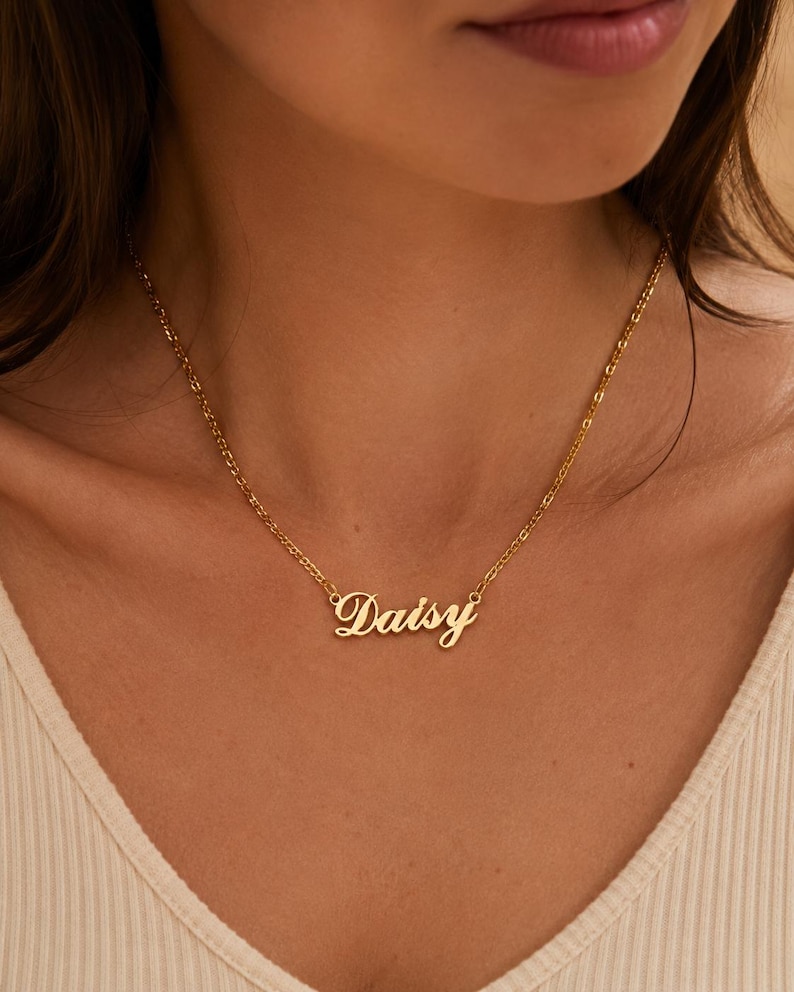Pu&ograve; includere: Una collana in metallo color oro con un ciondolo a forma di targhetta con il nome Daisy scritto in un carattere corsivo. Il ciondolo &egrave; fissato a una delicata catenina color oro che poggia attorno al collo, con una finitura lucida.