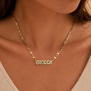 Pu&ograve; includere: Una collana color oro con un ciondolo rettangolare che riporta la parola QUEEN in un carattere a blocchi. Il ciondolo &egrave; fissato a una catena composta da maglie piatte, allungate e arrotondate che si uniscono per formare un design metallico strutturato.