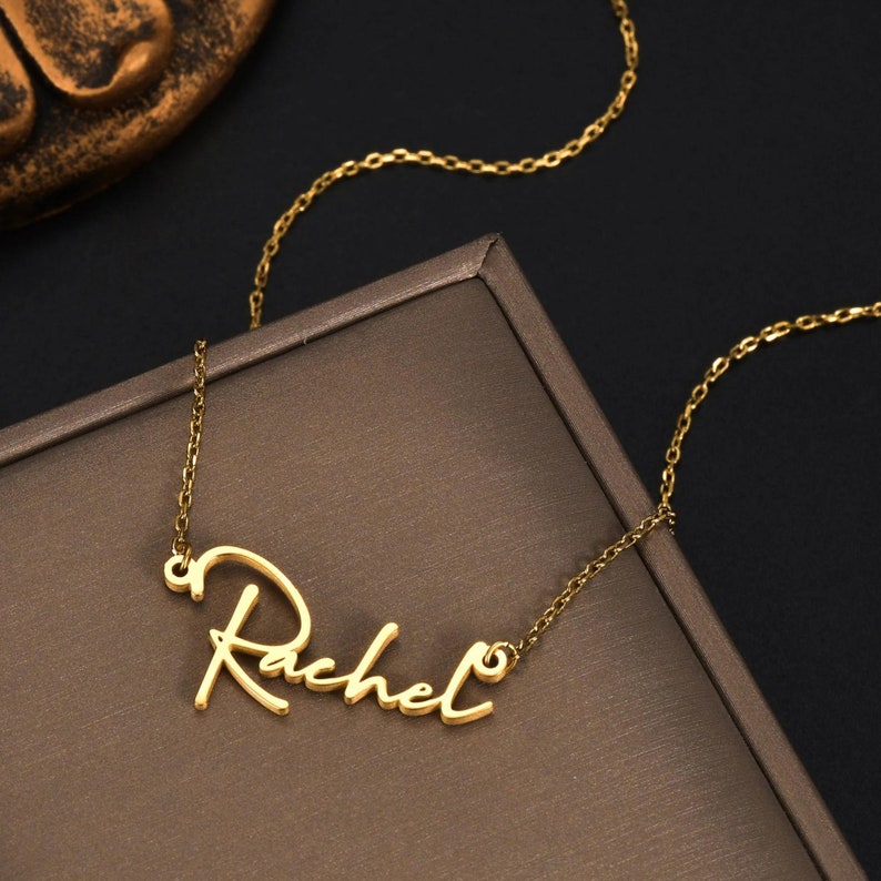 Pu&ograve; includere: Una collana color oro con un ciondolo a forma di targhetta con il nome Rachel scritto in corsivo. Il ciondolo &egrave; fissato a una delicata catenina color oro con piccoli anelli ovali, creando un gioiello continuo con una finitura lucida.