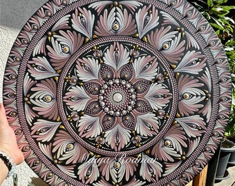May include: A round, decorative mandala with a detailed floral design. The artwork features a black background with pink, white, and gold accents. The design includes a central flower and radiating petal-like shapes. The artist's signature, "Darya Rodina", is visible.
