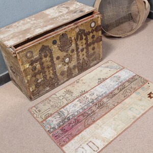 Könnte beinhalten: Eine antike Holzkiste mit aufwendigen Metalldetails und einem Teppich mit Blumenmuster. Die Kiste ist geöffnet und das Innere ist sichtbar. Der Teppich ist beige mit rosa und braunen Akzenten.