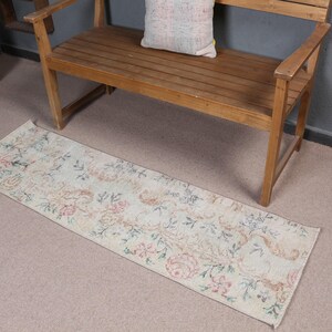 May include: A rectangular runner rug featuring a cream-colored base with a repeating floral pattern in muted shades of pink, blue, and green. The rug has a low-pile texture and displays a symmetrical arrangement of botanical motifs across its surface.