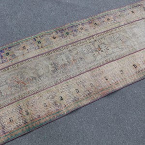 May include: A rectangular area rug featuring a faded, distressed pattern in muted beige, tan, and gray tones. The design includes horizontal bands with intricate, worn geometric motifs in accents of deep purple, teal, and orange throughout the weave.