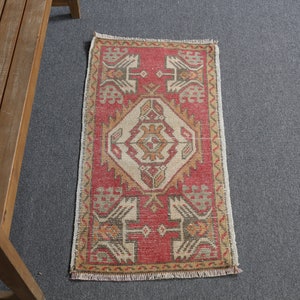 Könnte beinhalten: Ein kleiner, rechteckiger Teppich mit geometrischem Muster. Der Teppich hat einen roten Hintergrund mit beige- und braunfarbenen Akzenten. Das Design umfasst stilisierte Formen und ein zentrales Rautenmotiv. Der Teppich hat einen Fransenrand.