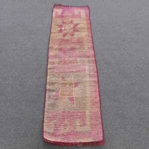May include: A long, narrow runner rug featuring a vibrant magenta and beige color palette. The rug displays geometric star motifs and linear patterns throughout its length, finished with short, fringed edges at both the top and bottom ends.