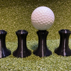May include: Four black plastic golf tee holders with a white golf ball on top of one of the holders.