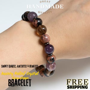 May include: A gemstone bracelet made with smoky quartz, amethyst, and hematite. The bracelet features a variety of brown, purple, and pink beads. The word "BRACELET" is displayed.