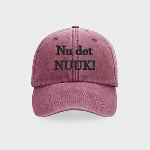 May include: A maroon baseball cap with the text "Nu det NUUK!" embroidered in black. The cap has a curved brim and a fabric strap closure.