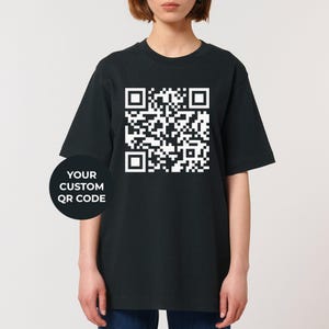 Pode incluir: Camiseta preta com um código QR branco impresso na frente. O texto "YOUR CUSTOM QR CODE" está impresso abaixo do código QR.