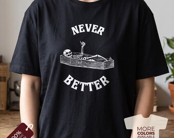 Puede incluir: Una camiseta negra de manga corta con un gráfico blanco de un esqueleto acostado en un ataúd de madera con una mano levantada. El texto NEVER está impreso sobre el ataúd y BETTER debajo en una fuente blanca en negrita.