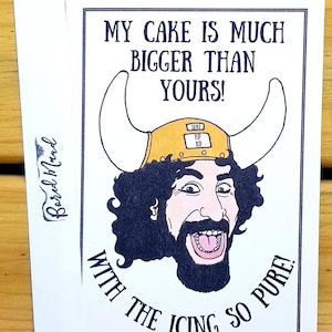 May include: A white greeting card featuring a cartoon illustration of a man in a horned helmet. The text says "MY CAKE IS MUCH BIGGER THAN YOURS! WITH THE ICING SO PURE!" The card is from Bored Mand.
