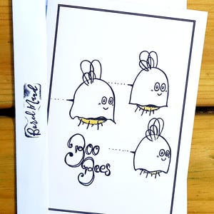 May include: A white greeting card with a black border features four cartoon bees with ghost-like bodies and the text "Boo Bees". The card is inside a white envelope with a black logo on the flap.