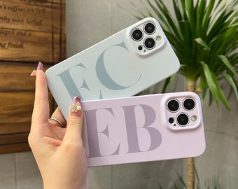 Può includere: Due custodie per telefono con iniziali personalizzate. La custodia superiore è blu chiaro con le iniziali "EC" in grigio chiaro. La custodia inferiore è viola chiaro con le iniziali "EB" in grigio chiaro. Entrambe le custodie hanno un ritaglio per l'obiettivo della fotocamera.