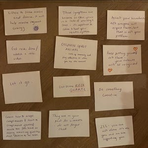 May include: A collection of handwritten notes on white paper, offering inspirational quotes and affirmations. The notes are arranged on a wooden surface, with messages like "Let it go" and "Do something creative."