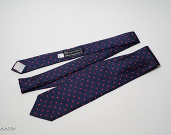 May include: A navy blue tie with red polka dots. The tie has a label that reads "The men's store Bloomingdale's".