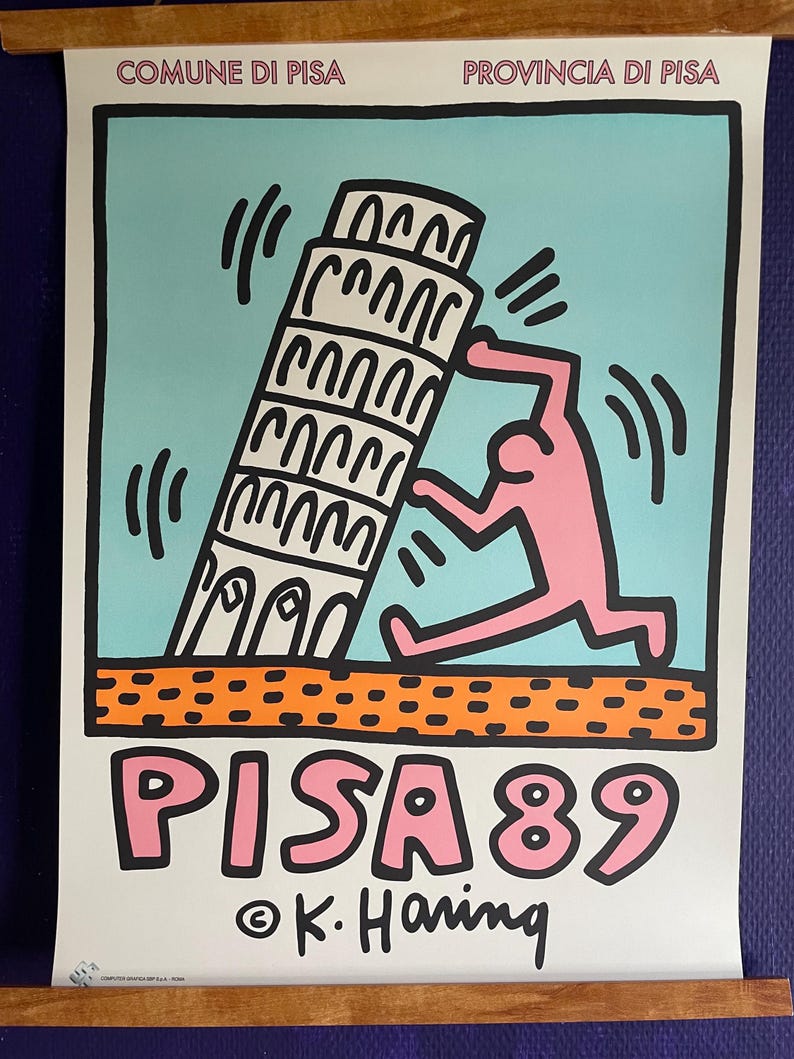 May include: A poster featuring a pink figure pushing the Leaning Tower of Pisa, with the text "PISA 89" in pink. The background is light blue, with orange and black accents. The artist's signature, K. Haring, is at the bottom.