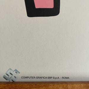 May include: Close-up of a framed artwork with a pink and black geometric shape. The artwork is set against a white background. The text "COMPUTER GRAFICA SBP S.p.A. - ROMA" is printed on the artwork.