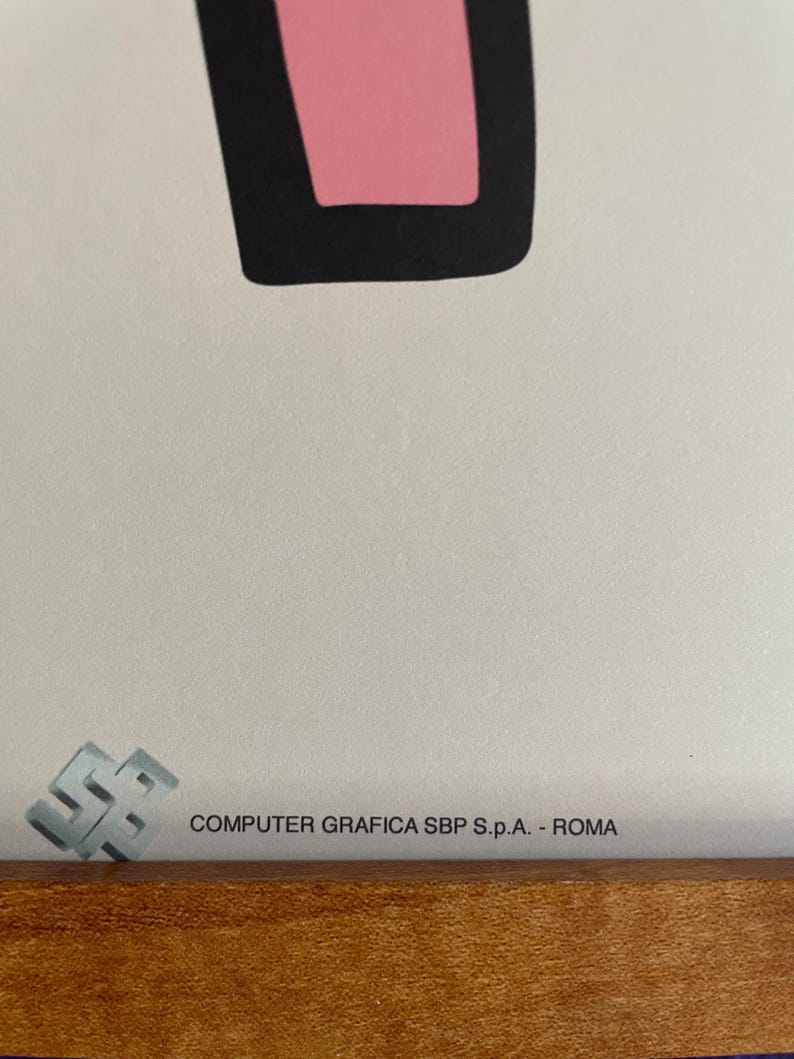 May include: Close-up of a framed artwork with a pink and black geometric shape. The artwork is set against a white background. The text "COMPUTER GRAFICA SBP S.p.A. - ROMA" is printed on the artwork.