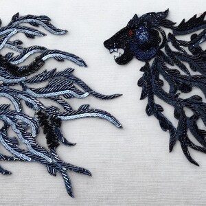 May include: Two lion head appliques. One is dark blue with silver and black accents, the other is black. Both have red eyes and are embellished with beads and sequins, creating a textured effect.