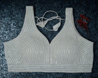 May include: Cream-coloured beaded top with a V-neck and tie-back. The top has vertical and diagonal beaded patterns, creating a textured effect. The garment is likely a blouse or crop top, suitable for formal or festive occasions.