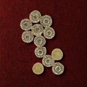 Op de afbeelding: Een decoratieve applicatie bestaande uit een groep van negen cirkelvormige, goudkleurige schijven in een onregelmatig patroon. Zeven van deze schijven zijn versierd met concentrische ringen van heldere, fonkelende strass-steentjes rond een centrale steen.