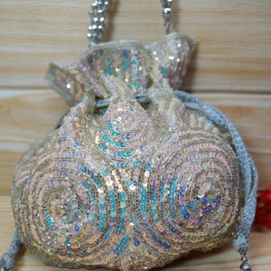 May include: A silver sequined drawstring bag with a silver chain strap and tassel. The bag is decorated with a swirling pattern of iridescent sequins.