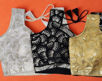 May include: Three sequined tops in silver, black, and gold, set against an orange backdrop. The tops feature a halter neckline and are adorned with detailed sequin designs. The silver top has white ties, the black top has black ties, and the gold top has a hanger.