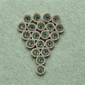 May include: A triangular brooch composed of twenty-one circular elements arranged in a cluster. Each element features a central peacock feather eye pattern in shades of green and blue, surrounded by a border of small, clear, reflective crystals.
