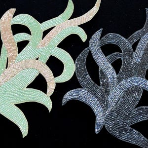 Peut inclure: Deux motifs décoratifs perlés sur fond noir. L'un est dans les tons de vert et de beige, l'autre dans les tons de gris et de bleu. Les motifs ont une forme organique et fluide, ressemblant à des feuilles ou des vignes stylisées.