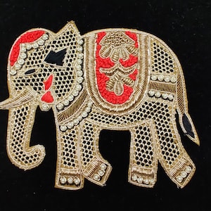 Könnte beinhalten: Gestickter Elefantenaufnäher mit Goldfaden, roten Akzenten und Kunstperlen. Der Elefant hat ein detailliertes Design mit einem roten Sattel und schwarzen Details. Dieser dekorative Aufnäher eignet sich für Kleidung oder Bastelprojekte.