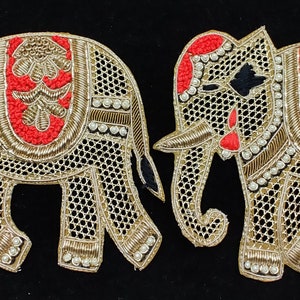 Könnte beinhalten: Zwei goldene bestickte Elefantenapplikationen mit roten und schwarzen Details. Die Elefanten sind mit Perlen verziert und haben ein traditionelles indisches Design.