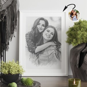 May include: A black and white pencil drawing of two women hugging. The drawing is framed in a white frame and is hanging on a white wall.