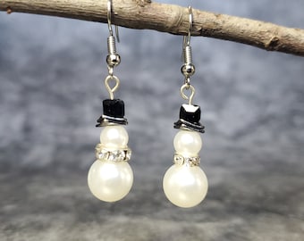 May include: A pair of silver snowman earrings with black hats and white pearl beads. The beads are accented with clear rhinestones.