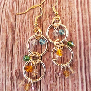 May include: Gold and silver dangle earrings with multiple small, colorful beads. The beads are in shades of green, blue, yellow, and purple.
