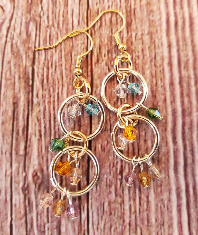 May include: Gold and silver dangle earrings with multiple small, colorful beads. The beads are in shades of green, blue, yellow, and purple.